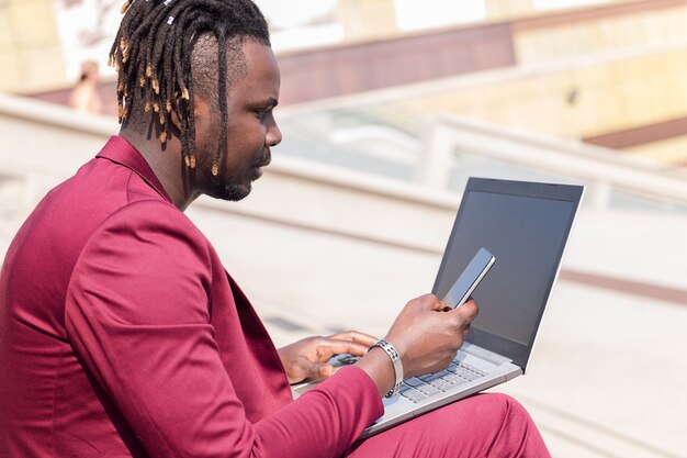 Photo un homme d'affaires noir élégant travaille à l'extérieur avec un ordinateur portable et un téléphone, une technologie et un concept de travail à distance