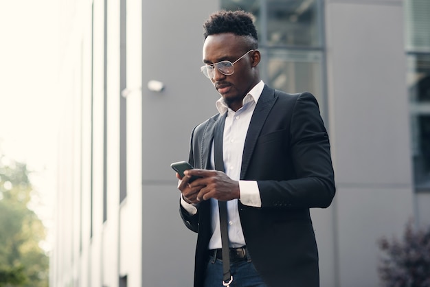 Homme d'affaires noir sérieux textos sur smartphone à l'extérieur