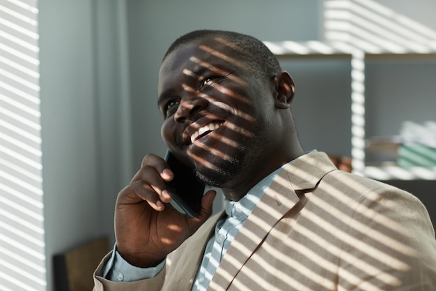 Homme d'affaires noir souriant parlant au téléphone au bureau avec la lumière du soleil