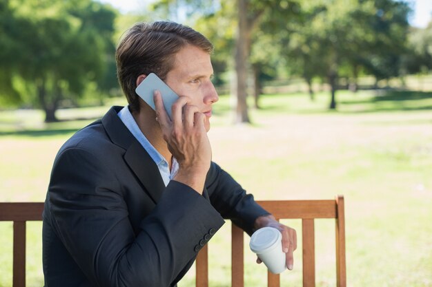 Homme d&#39;affaires occasionnel, parler au téléphone sur un banc de parc avec café