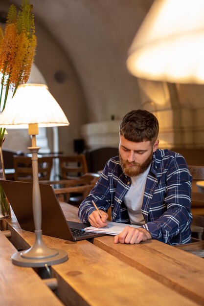 Homme d'affaires occasionnel ou pigiste planifiant son travail sur un ordinateur portable, travaillant sur un ordinateur portable avec un téléphone intelligent, une tasse de café sur une table au café ou au bureau à domicile, travaillant à partir du concept de café