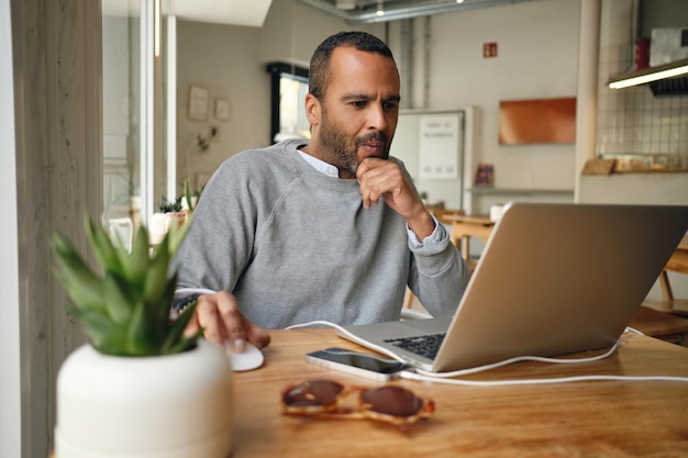 Homme d'affaires occasionnel travaillant intensément sur un ordinateur portable dans un café moderne. Homme réfléchi travaillant à l'intérieur