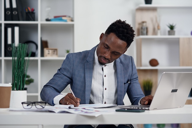 Homme d'affaires avec ordinateur portable. Jeune homme d'affaires africain tape quelque chose sur un ordinateur portable dans son bureau.