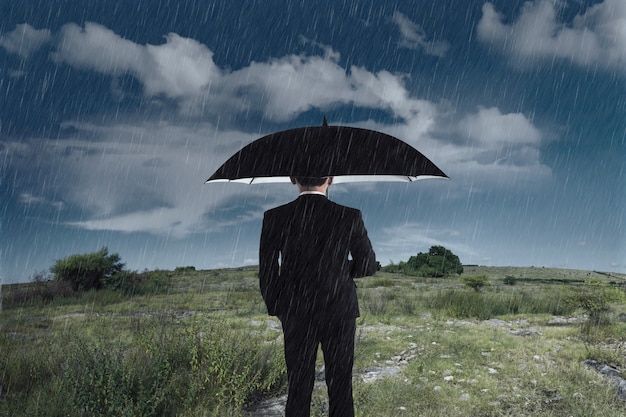 Homme d'affaires avec un parapluie debout sous la pluie