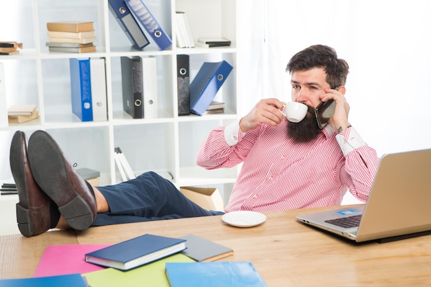 Un homme d'affaires parle sur un téléphone portable en buvant une tasse de thé dans un bureau moderne