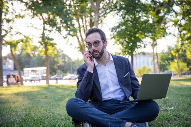 Un homme d'affaires passe un appel téléphonique tout en travaillant avec son ordinateur portable à l'extérieur