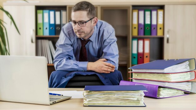 Homme d'affaires patron à son bureau au bureau avec un tas de dossiers