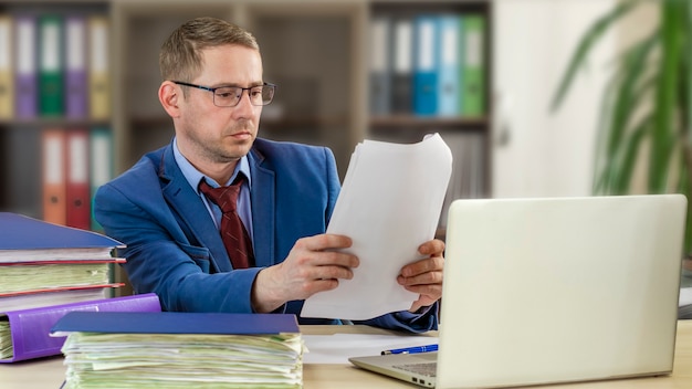 L'homme d'affaires de patron à son bureau dans le bureau examine des documents Contrôle financier