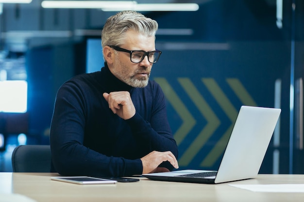 Homme d'affaires pensant à l'intérieur du bureau avec un ordinateur portable adulte mature patron pensant à la décision