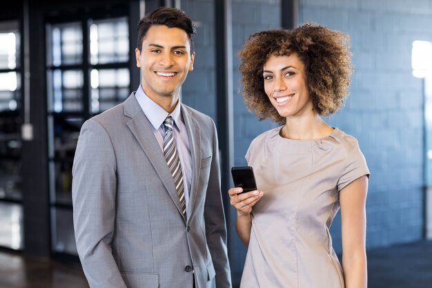 homme d&#39;affaires permanent avec jeune femme tenant un téléphone portable au bureau