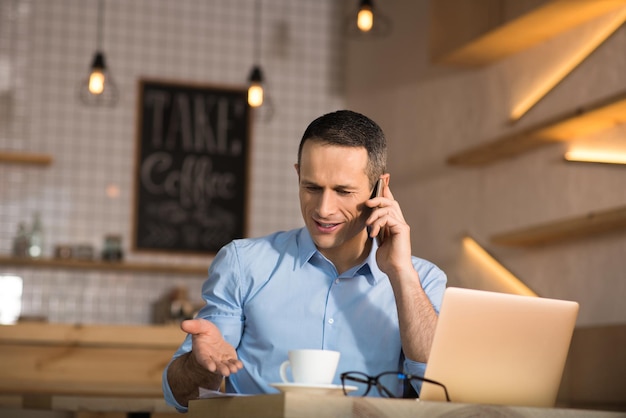 Homme d'affaires perturbé assis dans un café et parlant sur smartphone
