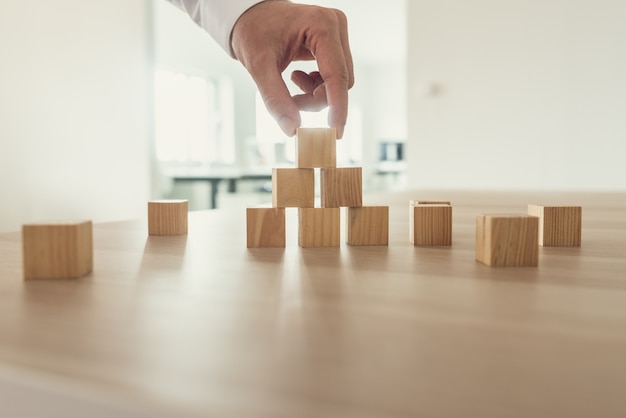 Homme d'affaires plaçant des cubes en bois en forme de pyramide sur un bureau sur son lieu de travail.