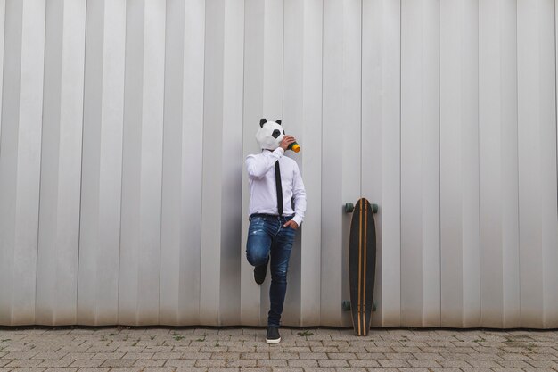 Homme d'affaires avec une planche à roulettes longboard et un masque d'ours panda prenant un café