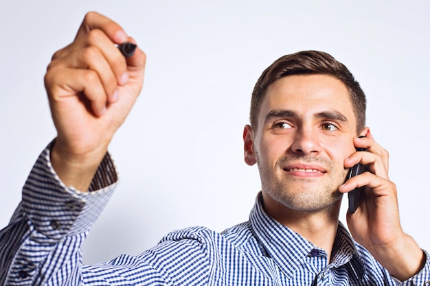 Homme d'affaires pointant quelque chose avec un marqueur et un téléphone portable sur fond blanc