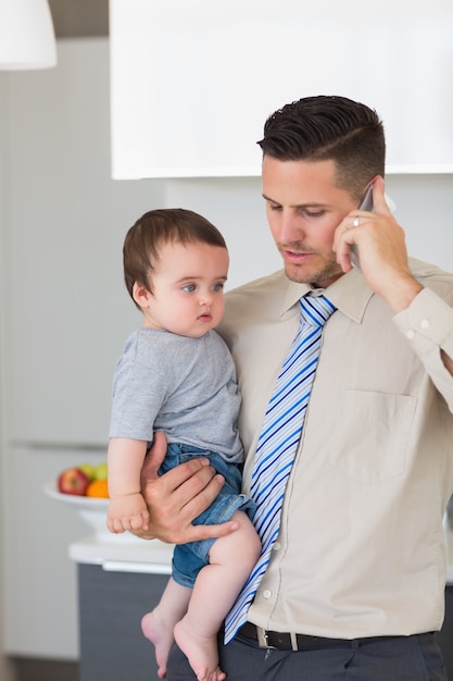 Homme d&#39;affaires portant bébé garçon tout en utilisant un téléphone mobile