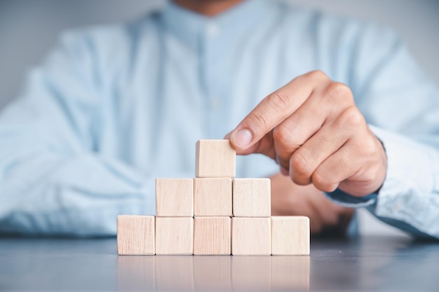 Homme d'affaires portant une chemise bleue arrangeant les blocs de bois vides avec ses mains Qui est placé sur une table en bois blanche Stratégie d'entreprise et plan d'action Espace de copie