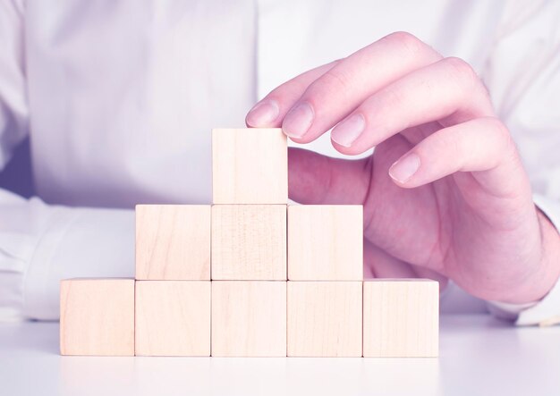 Homme d'affaires portant une chemise bleue arrangeant les blocs de bois vides avec ses mains Qui est placé sur une table en bois blanche Stratégie d'entreprise et plan d'action Espace de copie