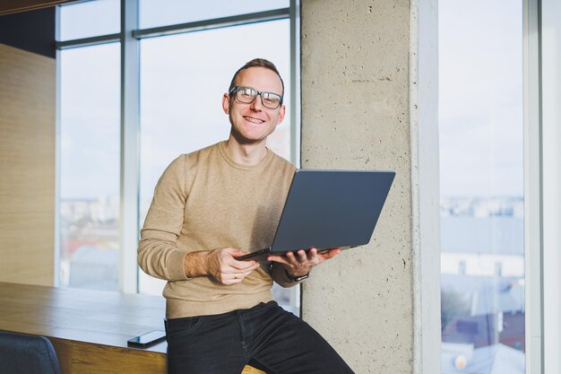 Un homme d'affaires portant des lunettes et des vêtements élégants boit du café dans un espace de travail moderne Un pigiste masculin avec un ordinateur portable travaille à distance