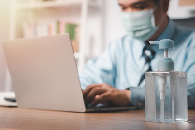 Homme d'affaires portant un masque et un désinfectant pour les mains sur son bureau pour la prévention du coronavirus