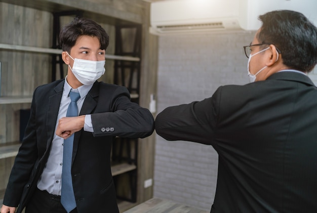 Homme D'affaires Portant Des Masques Protecteurs Saluant Les Coudes Se Cognant Sur Le Lieu De Travail. Protéger De Covid-19 Au Bureau. Concept De Soins De Santé