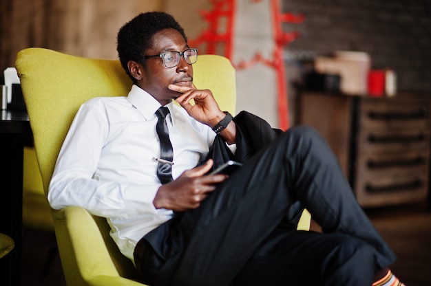 Photo homme d'affaires porter sur chemise blanche, cravate et lunettes au bureau, assis sur une chaise et tenant un téléphone mobile