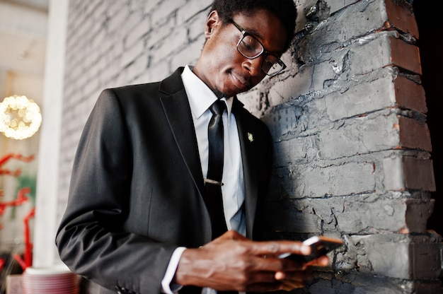 Homme d'affaires porter sur costume noir et lunettes au bureau à la recherche sur téléphone mobile