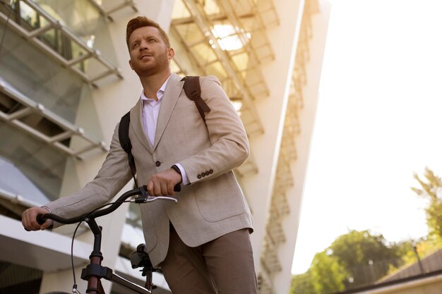 Homme d'affaires positif regardant au loin et debout avec un vélo dans la rue