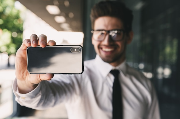 Homme d'affaires près du centre d'affaires à l'aide de téléphone portable, prendre un selfie.