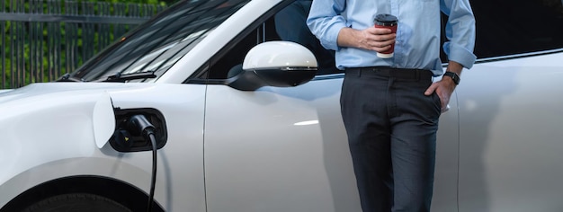 Homme d'affaires progressiste avec café et voiture EV à la station de charge