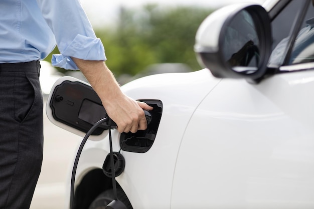 Un homme d'affaires progressiste en gros plan branche la prise du chargeur de la station de charge à l'EV