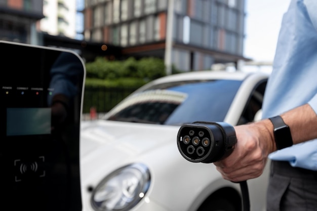 Un homme d'affaires progressiste en gros plan branche la prise du chargeur de la station de charge à l'EV