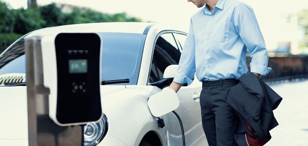 Un homme d'affaires progressiste en gros plan branche la prise du chargeur de la station de charge à l'EV