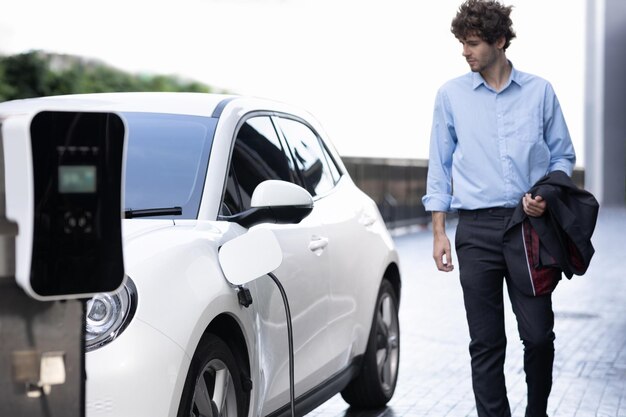 Homme d'affaires progressiste avec voiture EV à la station de recharge de voiture de stationnement public