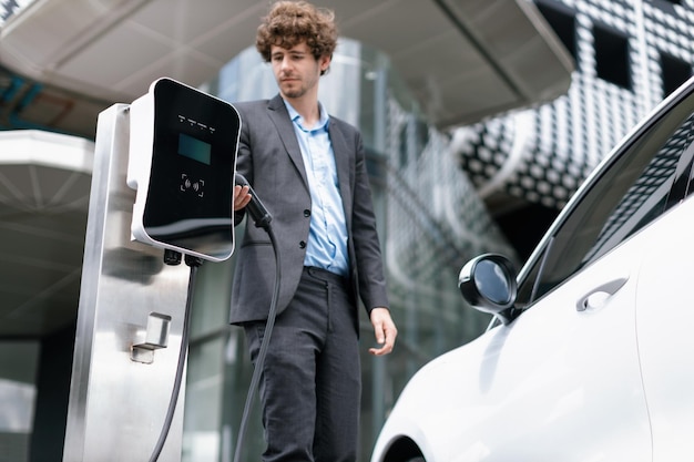 Homme d'affaires progressiste avec voiture EV à la station de recharge de voiture de stationnement public