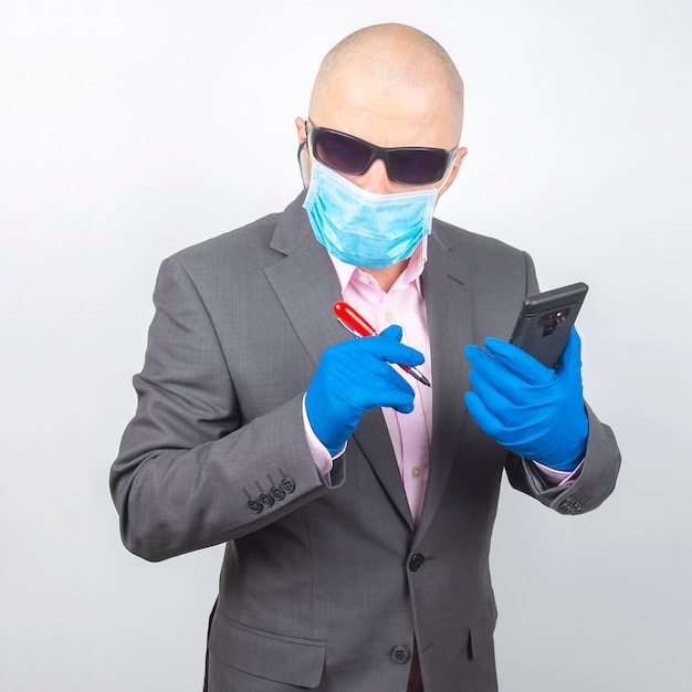 Un homme d'affaires prospère dans un masque de protection et des gants travaille sur un smartphone pendant la quarantaine du coronavirus. Travaillez en freelance en ligne.