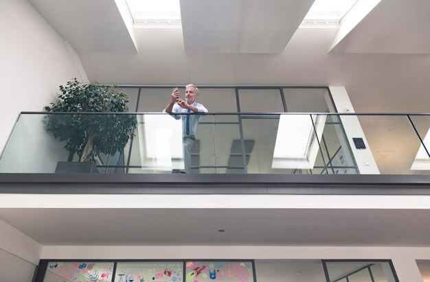 Homme d'affaires prospère debout à la balustrade de son bureau, à l'aide d'un smartphone