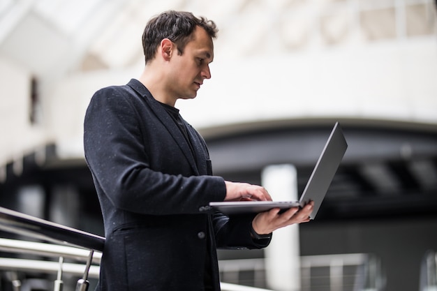 Homme d'affaires prospère, debout dans le centre de bureau tenant un ordinateur portable.