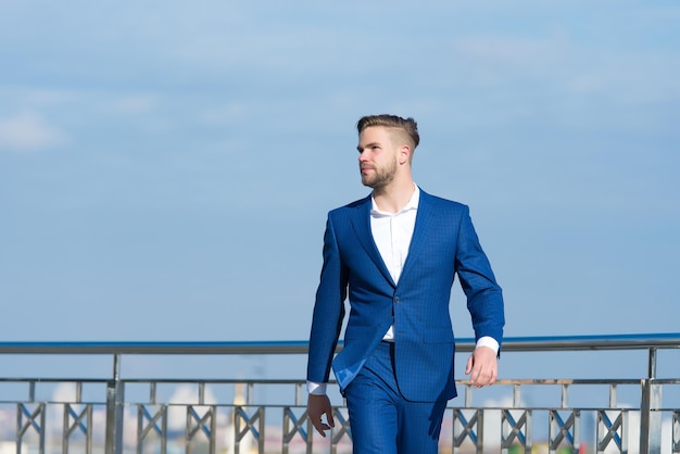 Homme d'affaires prospère entrepreneur en costume promenades en plein air journée ensoleillée, fond de ciel. L'homme confiant et bien soigné apprécie la liberté. Notion de liberté. L'apparence attrayante de l'homme d'affaires semble réussie.