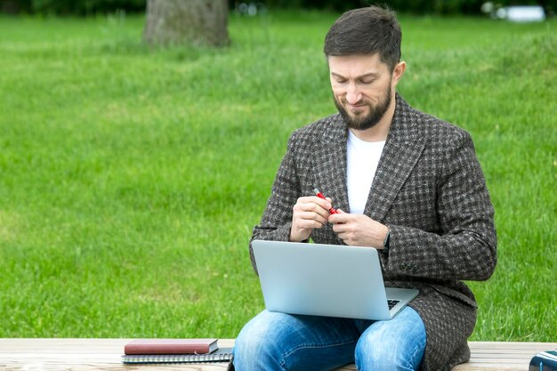 Un homme d'affaires prospère est assis sur un banc de la ville et est engagé dans des affaires avec des documents et un ordinateur portable