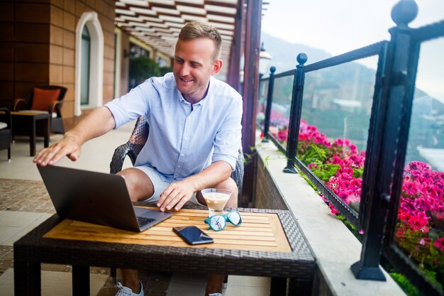 Un homme d'affaires prospère est assis à une table avec un ordinateur portable, il travaille en vacances. Vacances et télétravail. Le gars est assis dans un restaurant sur une terrasse avec vue panoramique