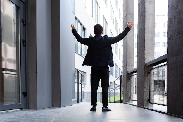 Un homme d'affaires prospère lève les mains en signe de victoire et de succès près de la vue arrière du bureau moderne