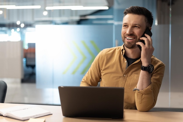 Homme d'affaires prospère parlant au téléphone portable assis sur le lieu de travail