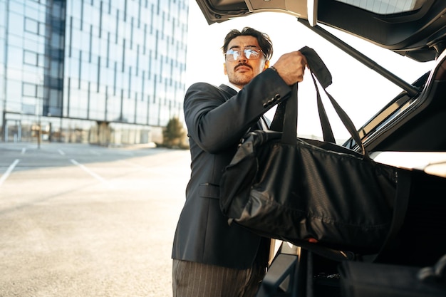 Homme d'affaires prospère prenant des bagages dans le coffre de la voiture