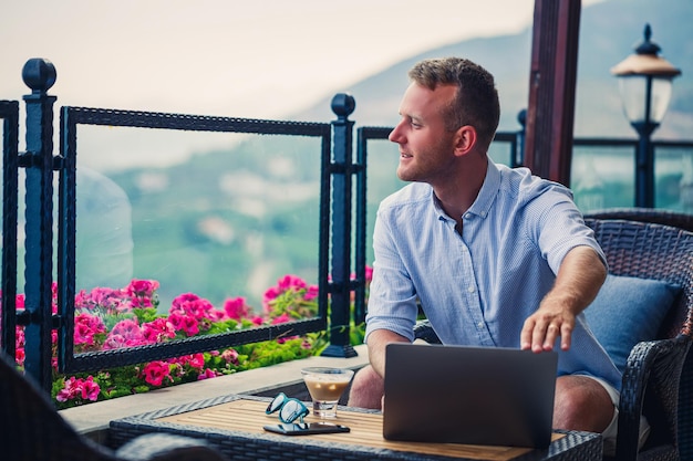 Homme d'affaires prospère travaillant en vacances derrière un ordinateur portable avec vue sur la montagne Flux de travail du gestionnaire en ligne Travaillez à l'extérieur avec une belle vue depuis le balcon