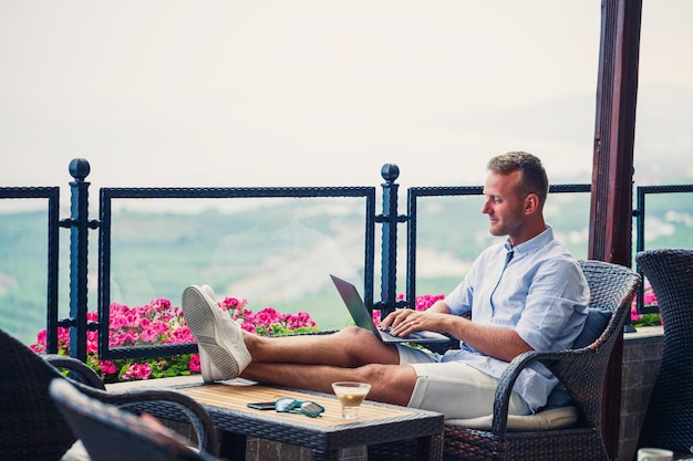 Homme d'affaires prospère travaillant en vacances derrière un ordinateur portable avec vue sur la montagne Flux de travail du gestionnaire en ligne Travaillez à l'extérieur avec une belle vue depuis le balcon