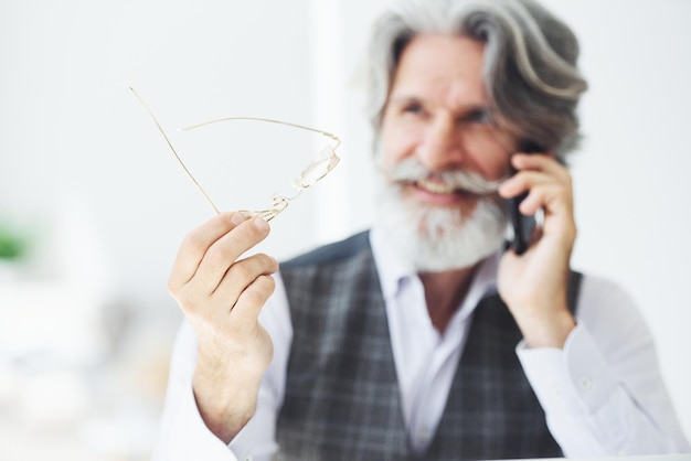 Homme d'affaires prospère utilise le téléphone Homme moderne et élégant aux cheveux gris et à la barbe à l'intérieur