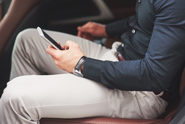 Un homme d'affaires qui envoie un message à un smartphone et se rend sur le siège arrière de la voiture.