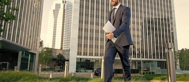 Homme d'affaires recadré en costume marchant avec un ordinateur portable à l'extérieur de l'entreprise agile de bureau