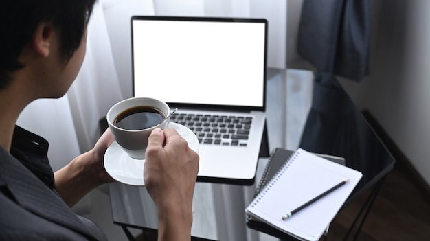 Homme d'affaires réfléchi buvant du café et utilisant un ordinateur portable dans la salle de bureau.