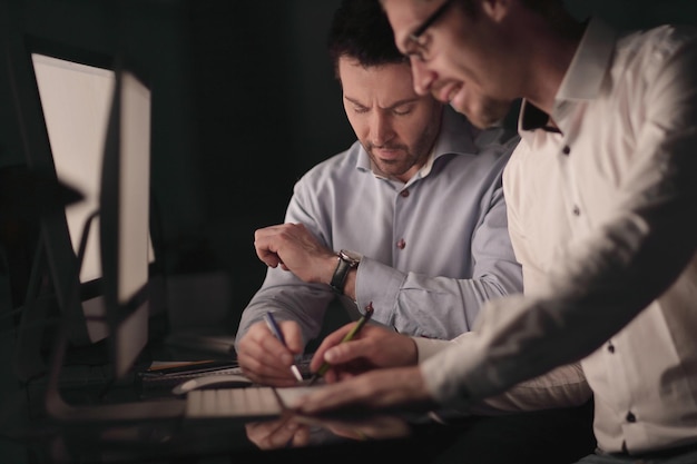 Homme d'affaires regardant sa montre alors qu'il était assis à son bureau le concept d'heures supplémentaires